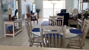 A dining area with a glass-top table, wooden chairs, a chandelier, and a view to the outside.