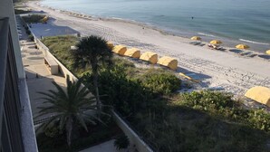 A beach with yellow umbrellas and lounge chairs, a sandy shore, and a clear view of the sea.