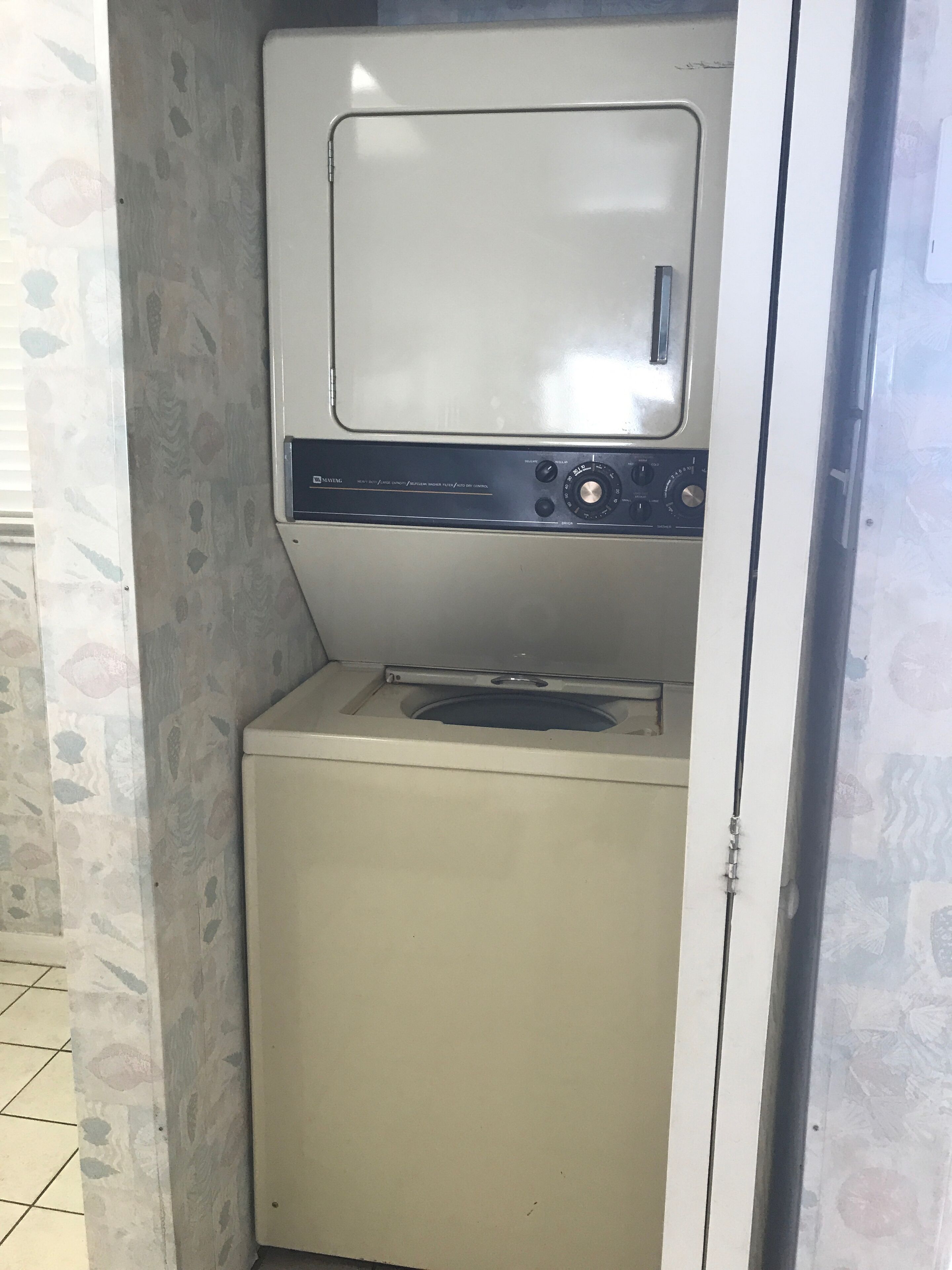 Una lavadora blanca y compacta con panel de control, ubicada en un pequeño lavadero cerrado con paredes decorativas.