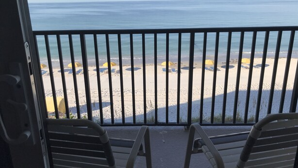 A balcony with metal railings overlooking a beach with yellow umbrellas and lounge chairs.