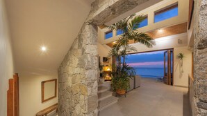 A spacious interior with a stone archway leading to a balcony overlooking the sea at sunset.