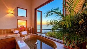 A bathroom with a bathtub, a sink, and a large window offering a view of the ocean.