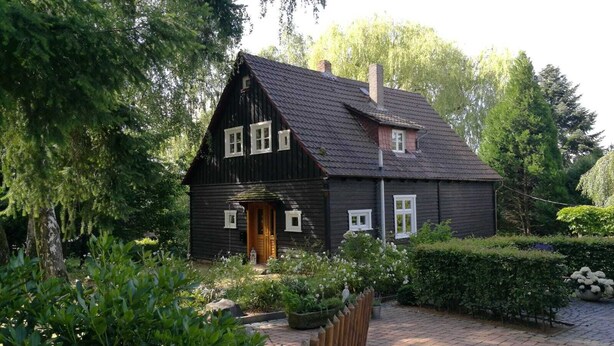 Ett mörkt trähus med ett sluttande tak, en trädörr och fönster med vita ramar.