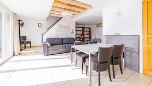 Un salon moderne avec un canapé gris, une table à manger et des chaises, ainsi qu’un escalier menant à un niveau supérieur.
