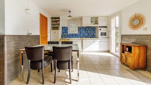 Une cuisine moderne avec un coin repas, comprenant un meuble en bois, un plan de travail blanc et une table à manger avec des chaises.