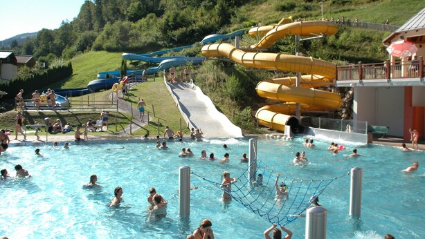 Une piscine dotée de plusieurs toboggans et d’une zone délimitée par un filet pour les jeux.