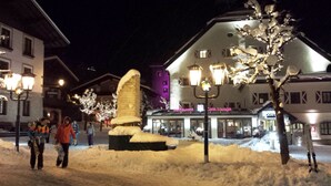 Une place enneigée, avec une grande sculpture de neige au centre, un restaurant et un café en arrière-plan.