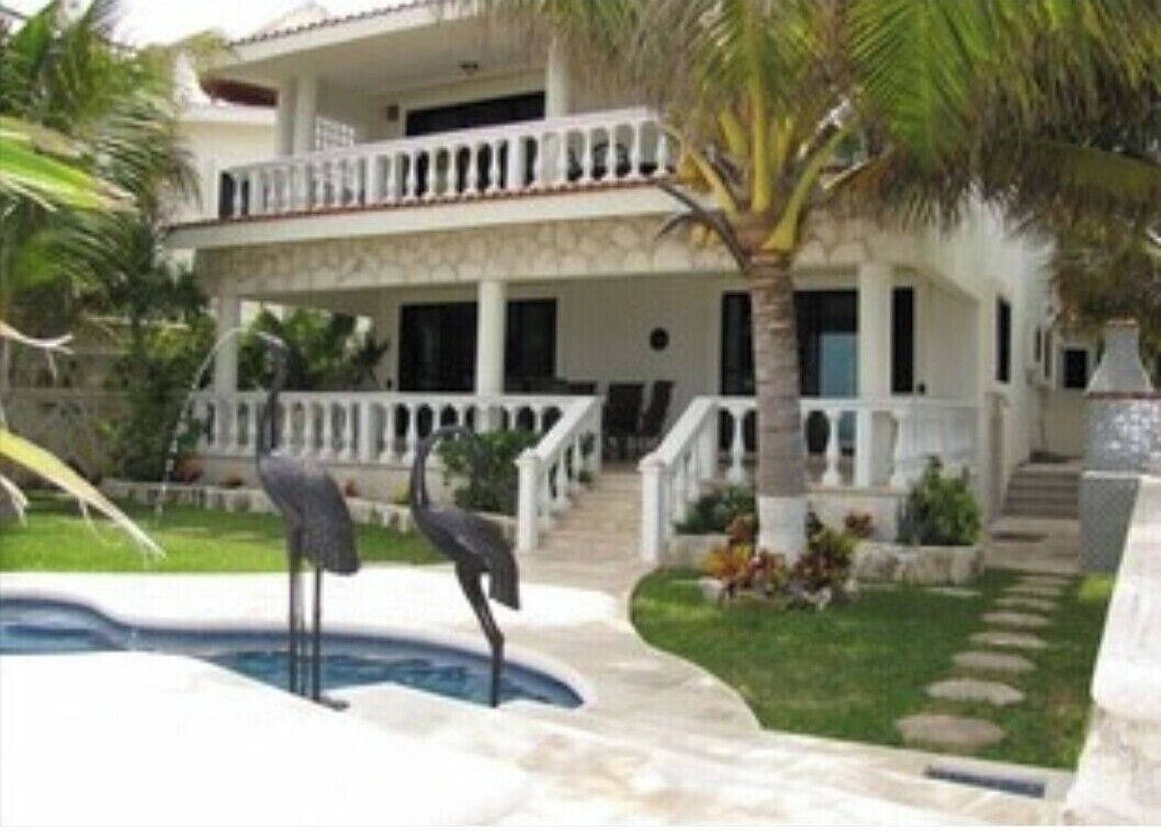 A two-story house with a balcony, a swimming pool, and a well-maintained garden with palm trees.
