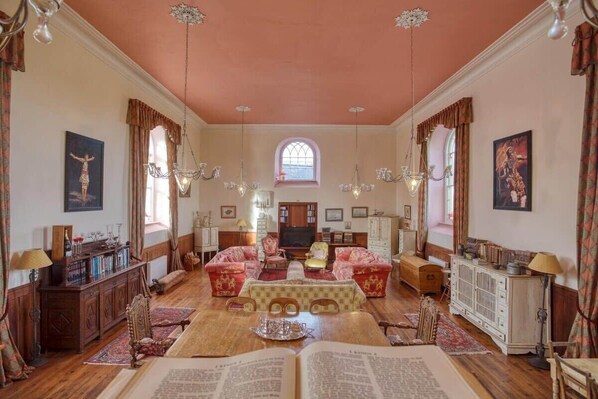 A spacious living room with a large window, multiple seating areas, and a television. - Historic Chapel, Great Facilities nr Beaches (St Austell)