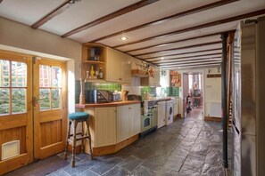 Cocina con vigas de madera, suelo de piedra y vista al jardín a través de la puerta.