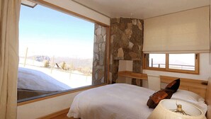 A bedroom with a large window, stone wall, and a bed with a pillow and lamp. - Ski Chalet Rental in Chile (Santiago)