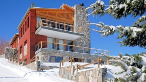 A modern multi-story building with a stone facade and wooden accents, featuring a balcony and a stone staircase leading to the entrance. - Ski Chalet Rental in Chile (Santiago)