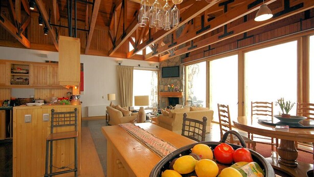 A spacious living area with a wooden dining table, a kitchen area, and a large window providing natural light. - Ski Chalet Rental in Chile (Santiago)
