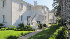 Un edificio residencial de dos pisos con fachada blanca, una escalera central y un césped bien cuidado.