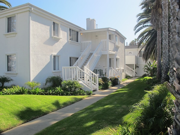 A two-story residential building with a white exterior, a central staircase, and a well-maintained lawn.