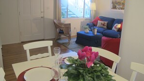 Un comedor con una mesa dispuesta para dos comensales, una silla y una maceta con flores rosadas.