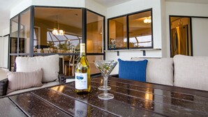 Une pièce avec un canapé, une table sur laquelle se trouve une bouteille de vin et un verre à martini, et de grandes fenêtres.