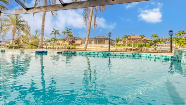 Une piscine à l’eau d’un bleu cristallin, entourée de palmiers et avec des maisons en arrière-plan.