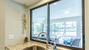 Une cuisine dotée d’un comptoir en granit, d’un évier en acier inoxydable et d’une grande fenêtre donnant sur un patio aménagé avec du mobilier d’extérieur.