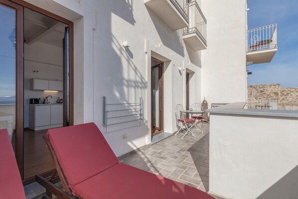 A balcony with red lounge chairs, a small table, and a view of the sea.