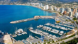 Un port de plaisance où sont amarrés de nombreux bateaux, entouré d’un paysage urbain côtier avec des montagnes en arrière-plan.