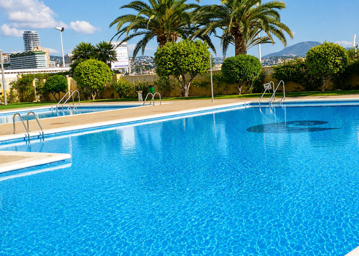 A clear blue swimming pool with a view of a cityscape in the background.