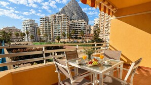 Un balcon avec une table préparée pour le petit-déjeuner, offrant une vue sur un paysage montagneux et des immeubles résidentiels.