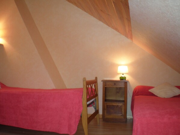 A small, cozy attic bedroom with two single beds, a nightstand with a lamp, and a wooden chair.