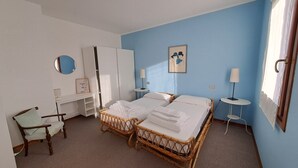 A hotel room with two single beds, a desk, a chair, a wardrobe, and a window with curtains.