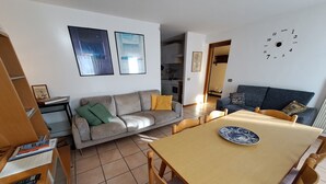 A modern living room with a sofa, a dining table, and a kitchen in the background.