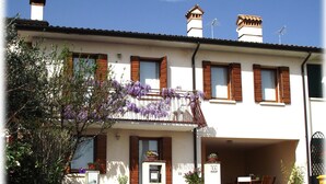 A two-story building with a balcony adorned with purple flowers, a garage, and a small outdoor seating area with chairs.