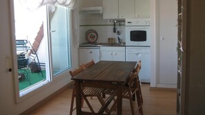 A kitchen with white cabinets, a wooden dining table, and a view through the window.