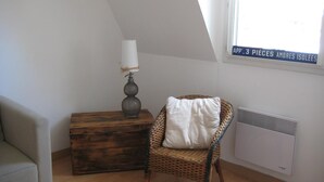 A cozy room with a wicker chair, a wooden chest, and a lamp.