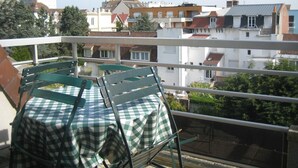 A balcony with a checkered table and chairs, overlooking a residential area with various buildings.