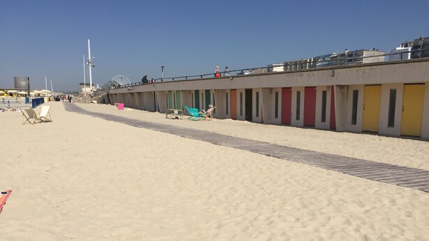 A beachside hotel with a row of rooms along the sand, a walkway, and a Ferris wheel in the background.