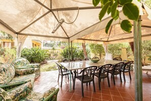 Un patio al aire libre con zona de comedor techada, sillas y una mesa.