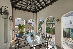 A covered patio with a glass table and chairs, surrounded by arches and potted plants.