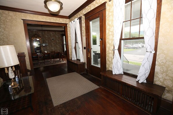 A hotel lobby with a wooden floor, a reception desk, a mirror, and a view of the outside.