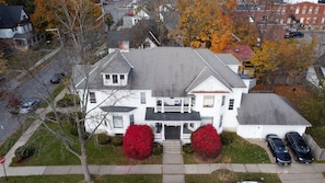 A large, two-story house with a front porch, a garage, and a driveway with cars parked.