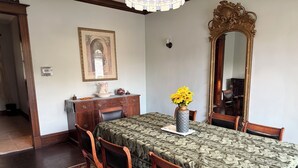 Een eetkamer met een tafel gedekt voor vier personen, een vaas met zonnebloemen, een grote spiegel en een lijst met een afbeelding aan de muur.