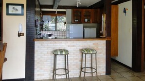Una cocina con una isla de ladrillo, dos taburetes de bar, armarios de madera y una lámpara colgante.