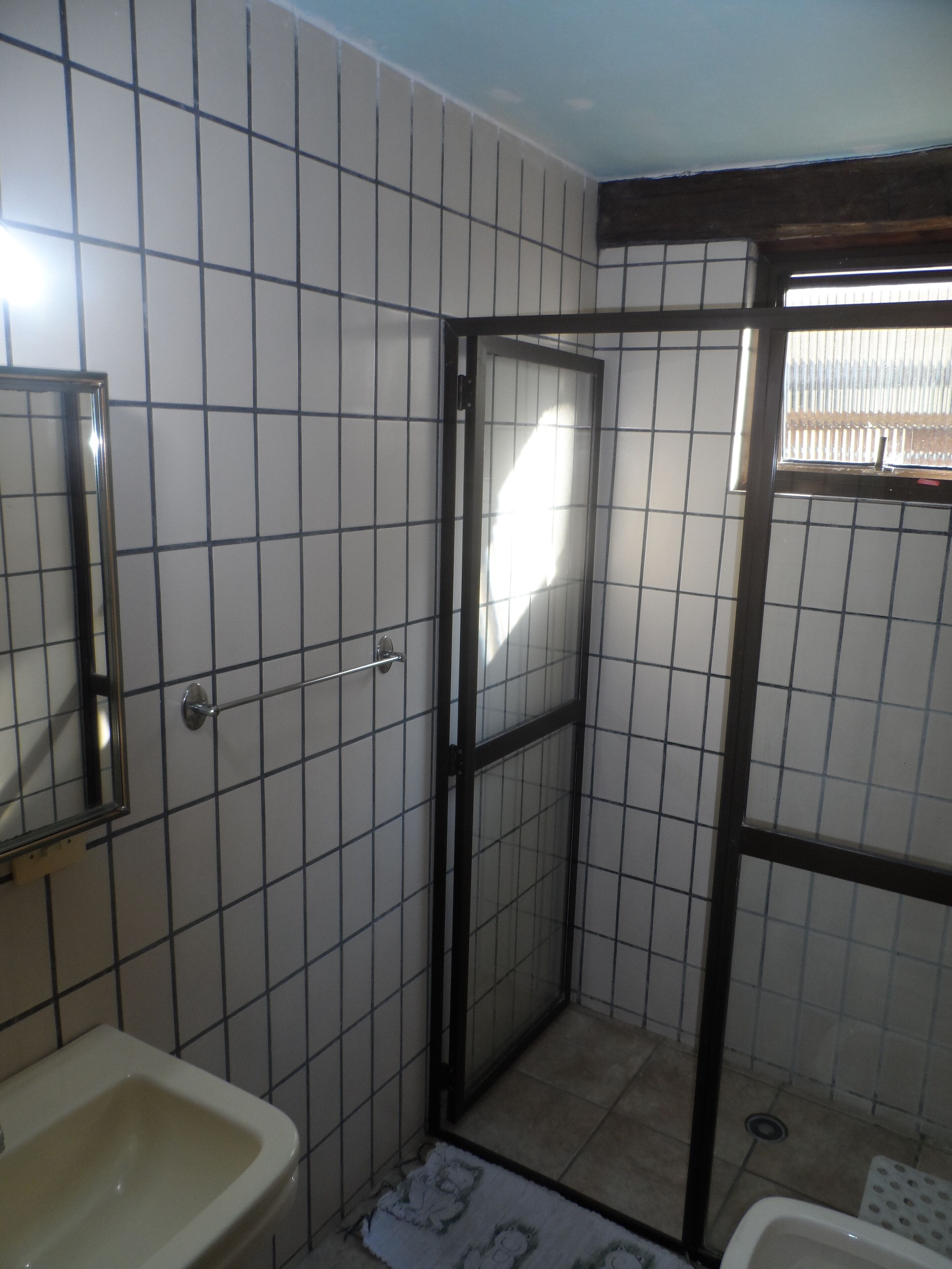 Ein Badezimmer mit Fliesenboden, Waschbecken, Spiegel und Duschbereich mit Glastür.