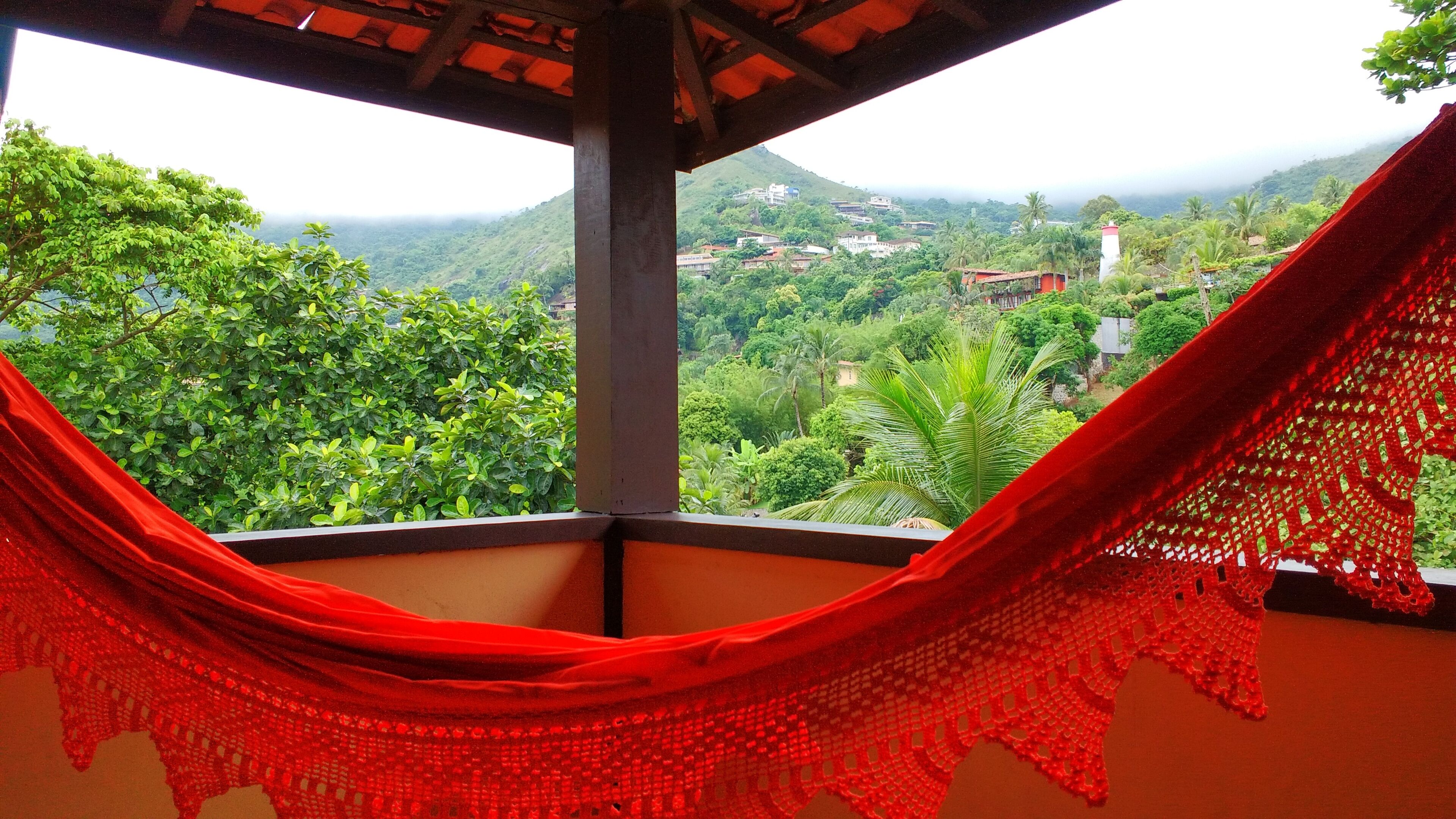 A hammock in a room with a view of a lush green landscape and a distant mountain range.