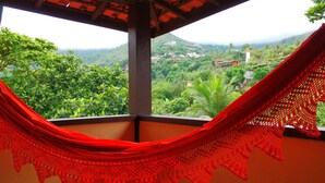Una hamaca en una habitación con vista a un paisaje verde exuberante y una cadena montañosa distante.