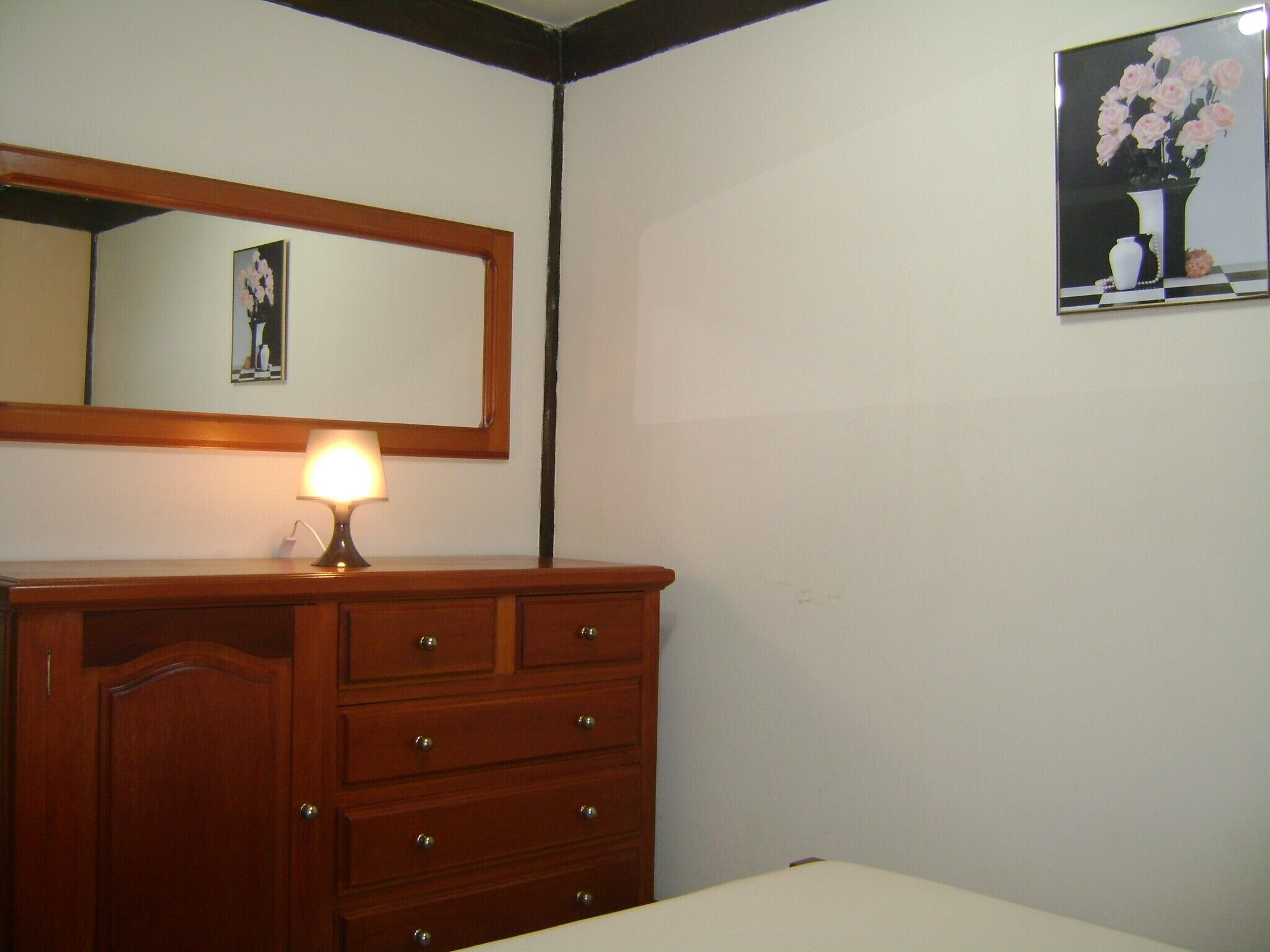 Un dormitorio con un aparador de madera, una lámpara de noche, una cama, un espejo y un cuadro en la pared.