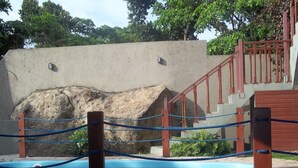 Una piscina con barreras de cuerda, un muro de hormigón y una escalera con barandillas rojas.