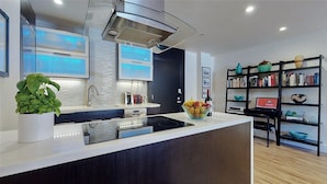 A modern kitchen with a central island, stainless steel appliances, and a black bookshelf with decorative items. - Centrally Located Modern Luxury, Walking Distance to UCLA, Westwood (Los Angeles)