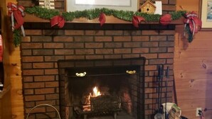 A brick fireplace with a lit fire, a framed picture above it, and a dog bed with a small dog inside. - A Little Slice of Smokey Mtn. Heaven - with WIFI (Franklin)