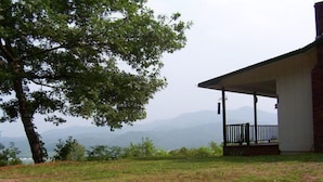 A building with a covered porch, a tree in the foreground, and a mountainous backdrop. - A Little Slice of Smokey Mtn. Heaven - with WIFI (Franklin)