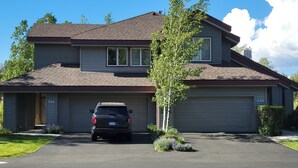 Une maison à deux étages avec un garage, une allée et un arbre devant.